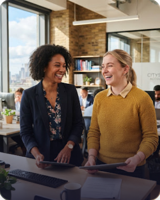 Two happy professional female colleagues laughing in office space